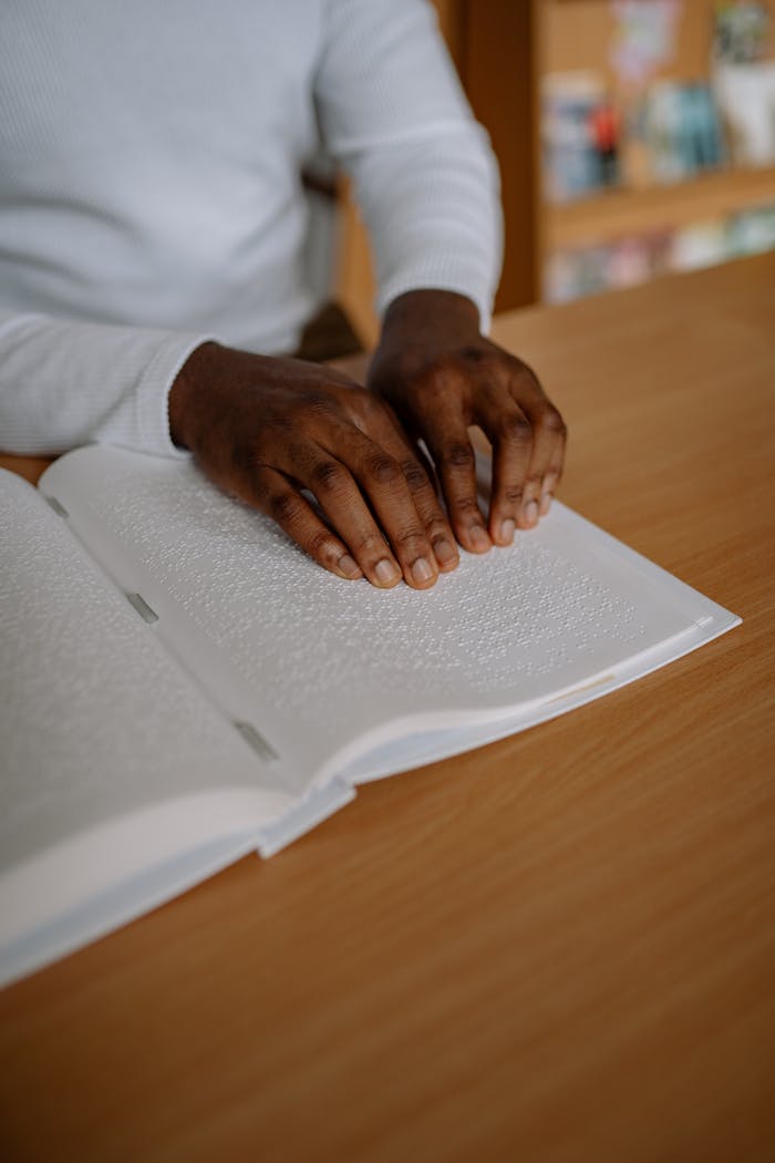 Close up of a Person Reading a Braille Book on a Desk